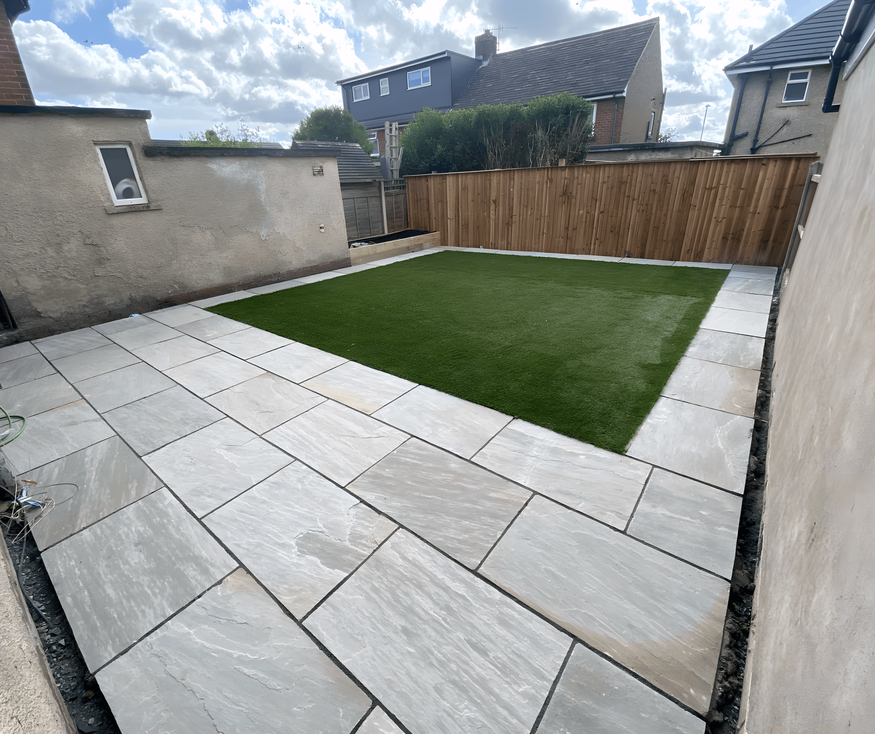 Corner of a garden with a slab patio, artificial grass and timber fence